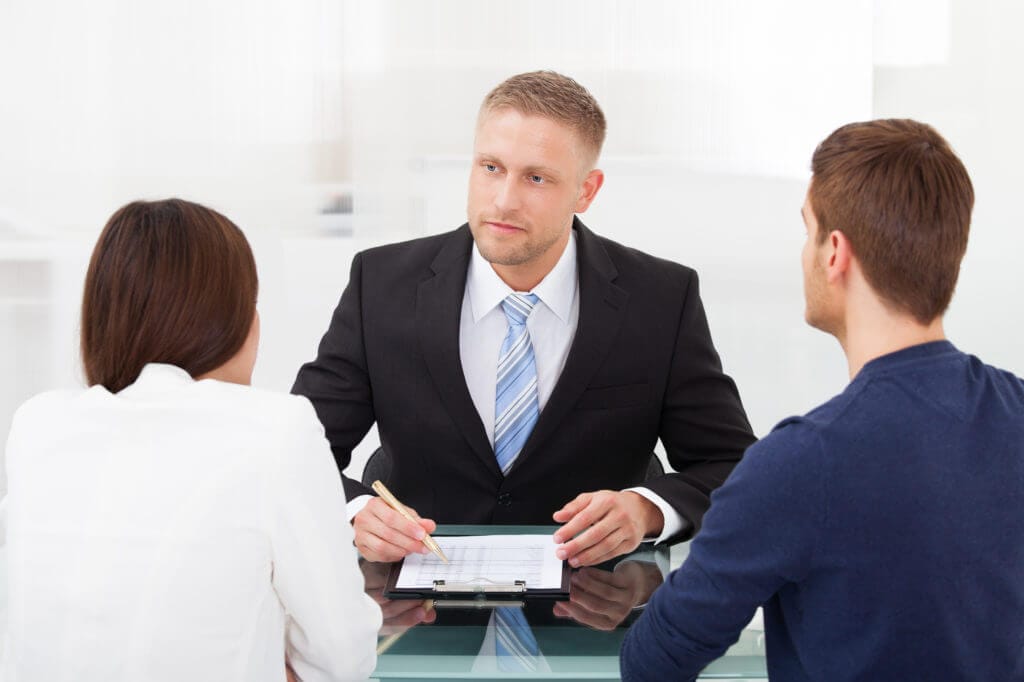 A professional attorney in a tailored suit sits at a sleek conference table, reviewing detailed estate planning documents with an attentive couple in a bright, modern office filled with law books and natural light.